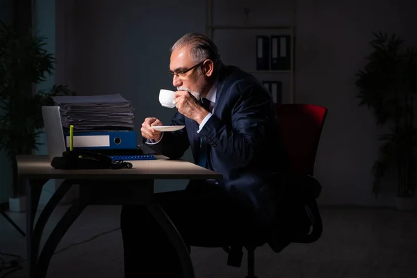 Oude mannelijke werknemer die laat op de werkplek werkt — Stockfoto