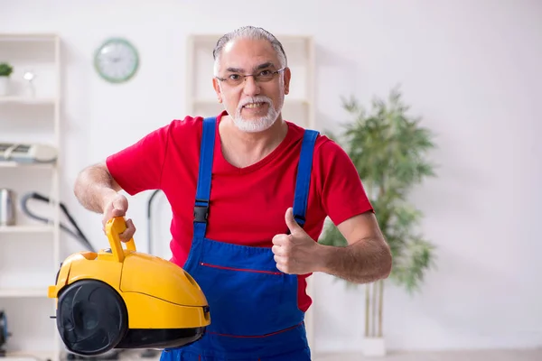 Vecchio appaltatore di sesso maschile riparazione aspirapolvere all'interno — Foto Stock