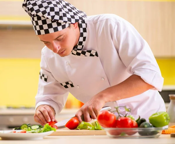 Young professional cook preparing salad at kitchen