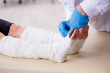 Genç bacak yaralı kadın yaşlı doktor travmatoloğu ziyaret ediyor.