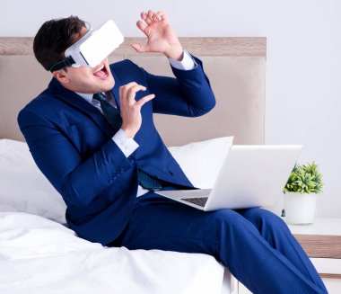 Yatak odasında sanal gerçeklik kulaklığı takan bir iş adamı.