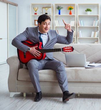 Evde gitar çalan bir iş adamı.