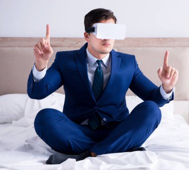 Yatak odasında sanal gerçeklik kulaklığı takan bir iş adamı.