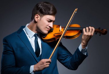 Genç adam karanlık odada keman çalıyor.