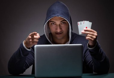 Kapüşonlu genç adam dizüstü bilgisayarın önünde oturuyor.