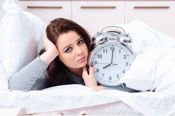 Νεαρή γυναίκα ξαπλωμένη στο κρεβάτι στη διαχείριση του χρόνου έννοια — Φωτογραφία Αρχείου