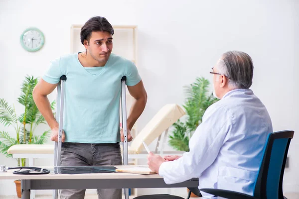 Genç bacağı yaralı erkek hasta yaşlı doktoru ziyaret ediyor. — Stok fotoğraf