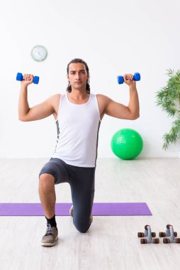 Genç yakışıklı adam içeride spor yapıyor.