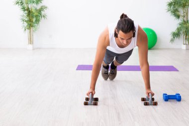 Genç yakışıklı adam içeride spor yapıyor.