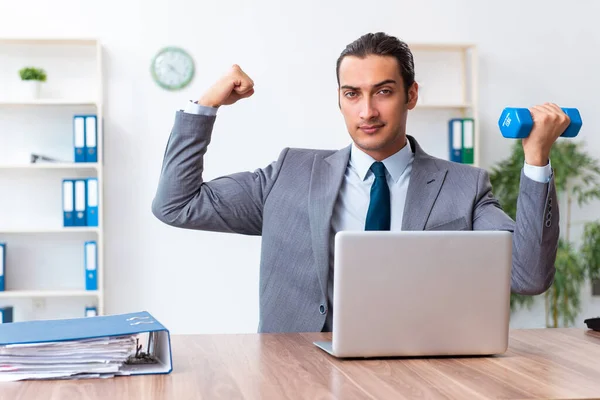 Jovem e bonito funcionário fazendo exercícios esportivos no local de trabalho — Fotografia de Stock