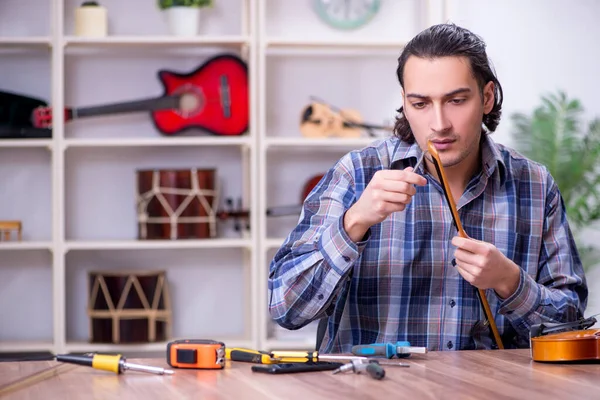 Молодой красивый ремонтник чинит скрипку — стоковое фото