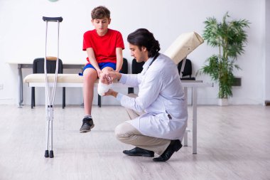 Genç doktor travmatoloğu ziyaret eden bacağı yaralı bir çocuk.