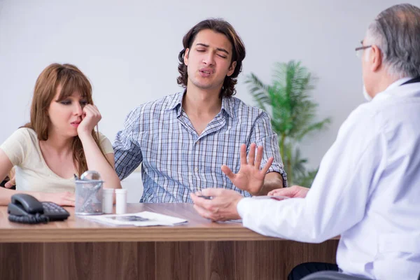 Pareja joven visitando viejo médico masculino — Foto de Stock