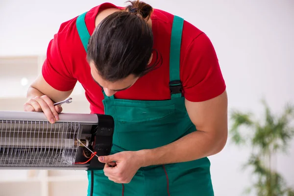 Young male contractor repairing heater indoors