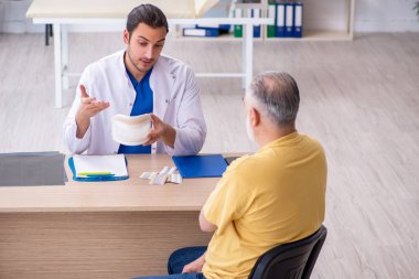 Yaşlı boynu yaralı bir adam genç erkek doktoru ziyaret ediyor.