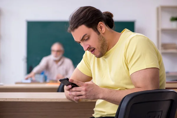 Old teacher and young male student in the classroom