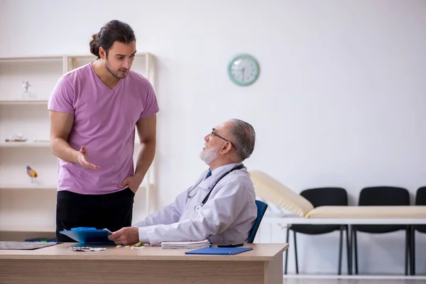 Junge männliche Patientin besucht alten männlichen Arzt — Stockfoto