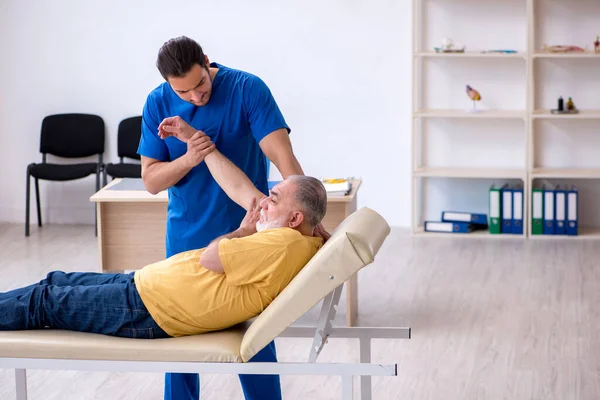 Vecchio ferito visitando giovane medico chiropratico maschile — Foto Stock