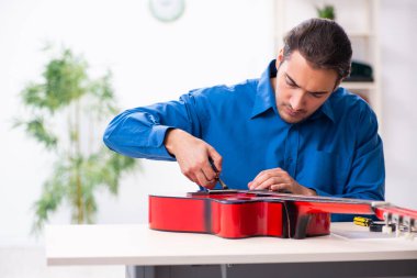 Gitarı tamir eden genç bir erkek tamirci.