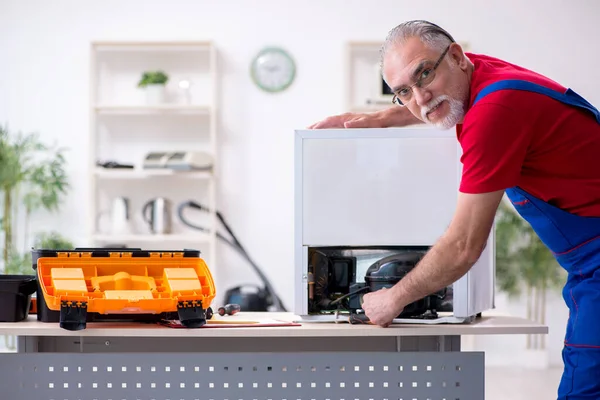 Old male contractor repairing refrigerator indoors — Stock Photo, Image