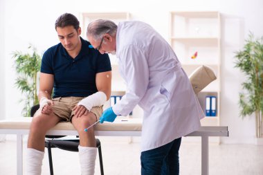 Genç yaralı adam yaşlı doktor travmatoloğu ziyaret ediyor.
