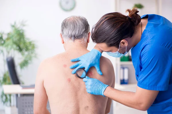 Homem velho visitando jovem médico dermatologista masculino — Fotografia de Stock