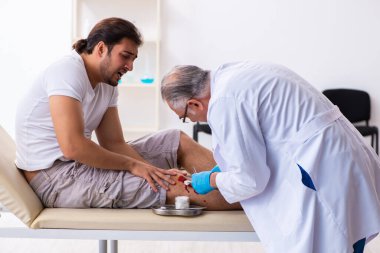Yaralı adam ilk yardım konseptinde yaşlı doktoru ziyaret ediyor.