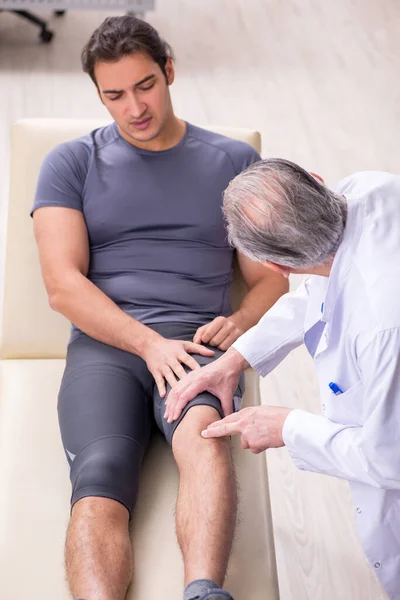 Joven paciente masculino visitando al viejo médico traumatólogo — Foto de Stock