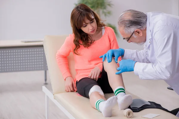 Jovem perna ferida mulher visitando médico velho traumatologista — Fotografia de Stock