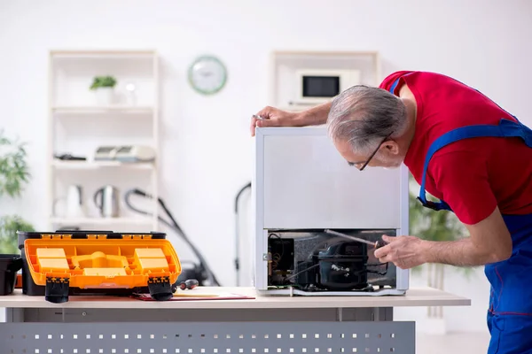 Velho empreiteiro masculino reparando geladeira dentro de casa — Fotografia de Stock