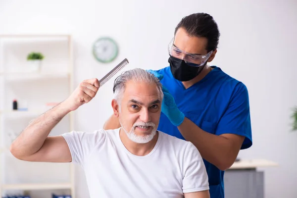 Old man visiting young male doctor in hair transplantation conce