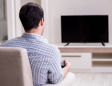 Genç adam evde televizyon izliyor.