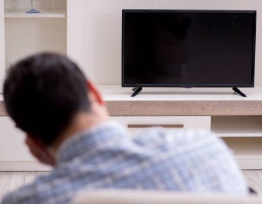 Genç adam evde televizyon izliyor.