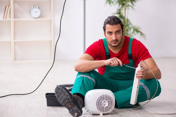 Young male contractor repairing fan heater indoors