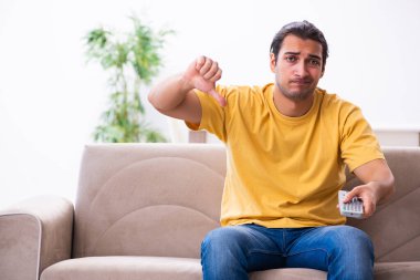 Genç adam evde televizyon izliyor.