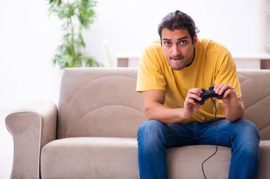 Genç adam evde joystick oynuyor.