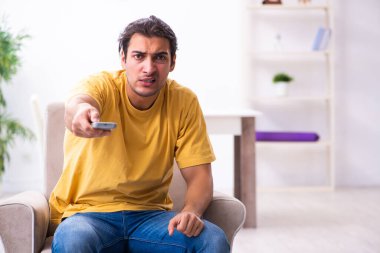 Genç adam evde televizyon izliyor.