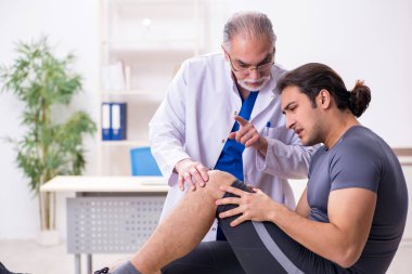Genç erkek hasta yaşlı doktor travmatoloğu ziyaret ediyor.