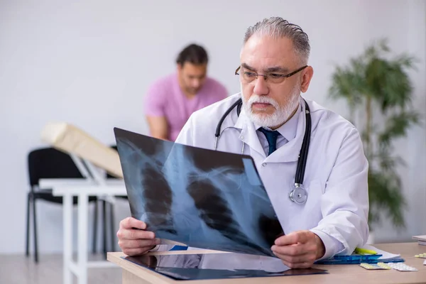 Старый врач-рентгенолог осматривает молодого пациента — стоковое фото