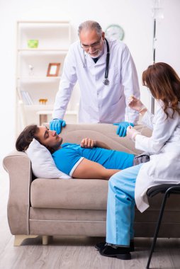 İki doktor hasta bir genci ziyaret ediyor.
