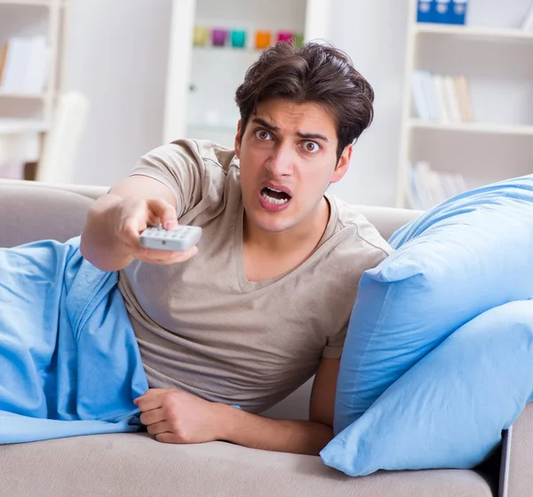 Hombre viendo la televisión desde la cama sosteniendo la unidad de control remoto — Foto de Stock