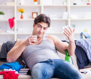 Dağınık bir odada alkol alan genç bir öğrenci.