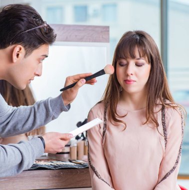 Güzellik salonunda güzel bir kadın için makyaj yapan adam.