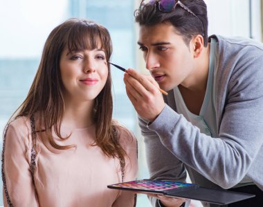 Güzellik salonunda güzel bir kadın için makyaj yapan adam.