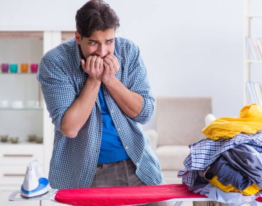 Genç adam evde çamaşır ütülüyor.