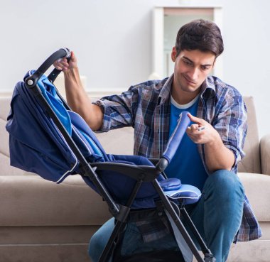 Genç baba evde bebek arabası monte ediyor.