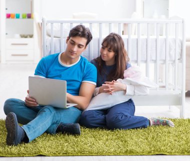 Yeni doğmuş bebekleriyle halıda oturan genç ebeveynler.