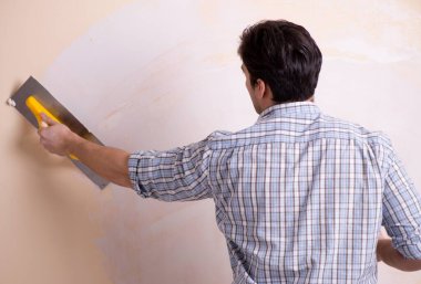 Evdeki duvara alçı yapıştıran genç adam.