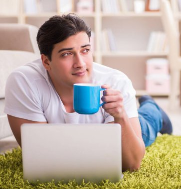 Evde, halı döşemesinde dizüstü bilgisayarda çalışan bir adam.