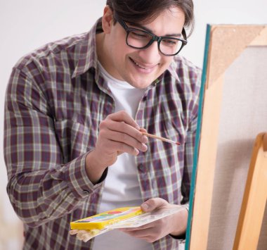 Genç erkek sanatçı parlak stüdyoda resimler çiziyor.